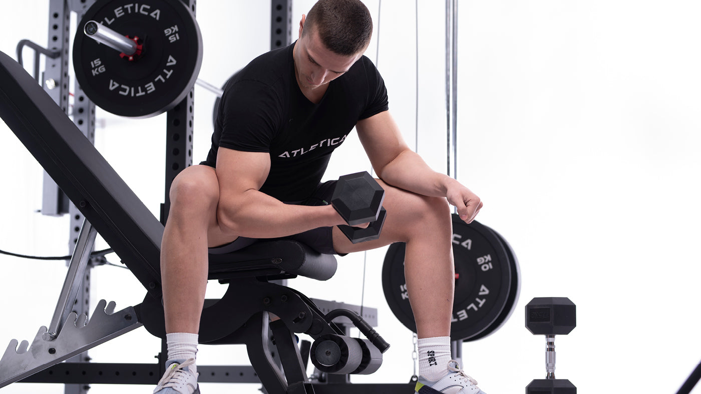 Mężczyzna wykonuje ćwiczenia na biceps heksagonalną hantlą ATLETICA na skośnej ławce
