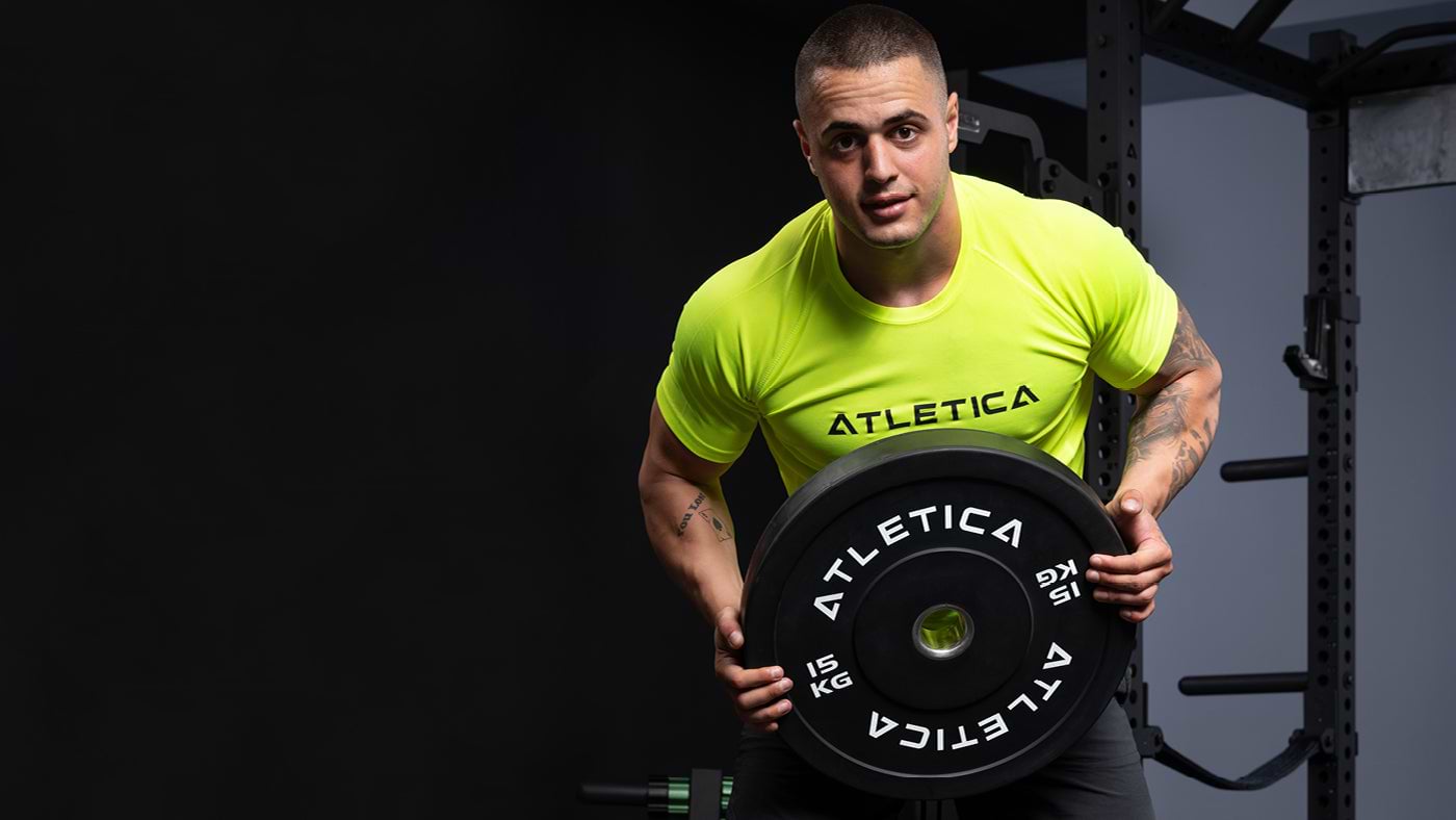 Karlos Nasar houdt een zwarte Atletica bumperschijf van 15 kg vast