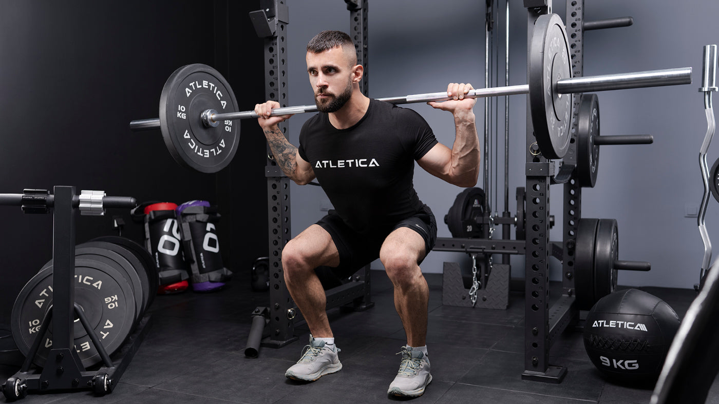 Back squat met Atletica halterstang en grijze gekleurde bumperschijven in de thuisgym