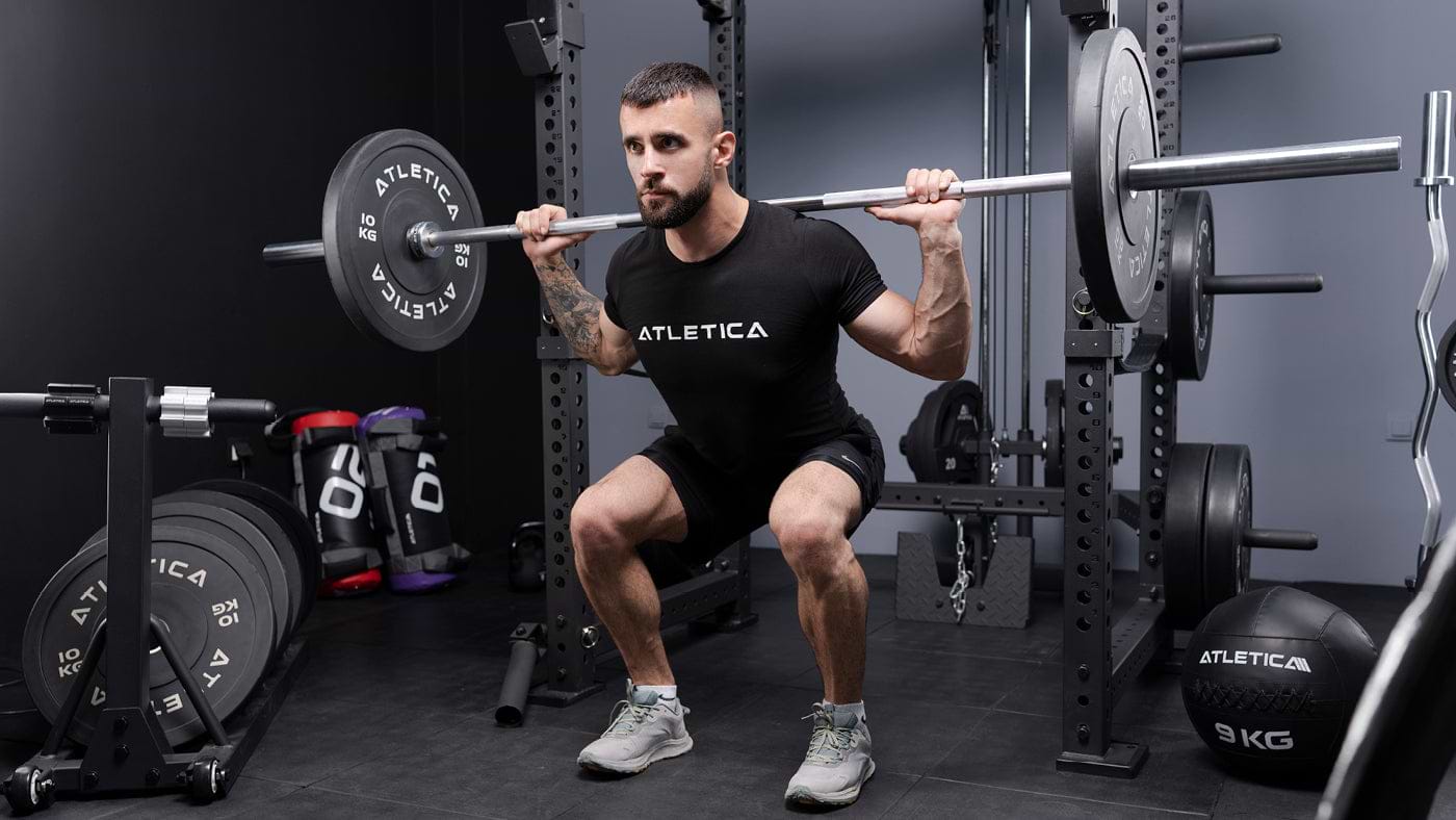 Back squat met Atletica halterstang en grijze gekleurde bumperschijven in de thuisgym