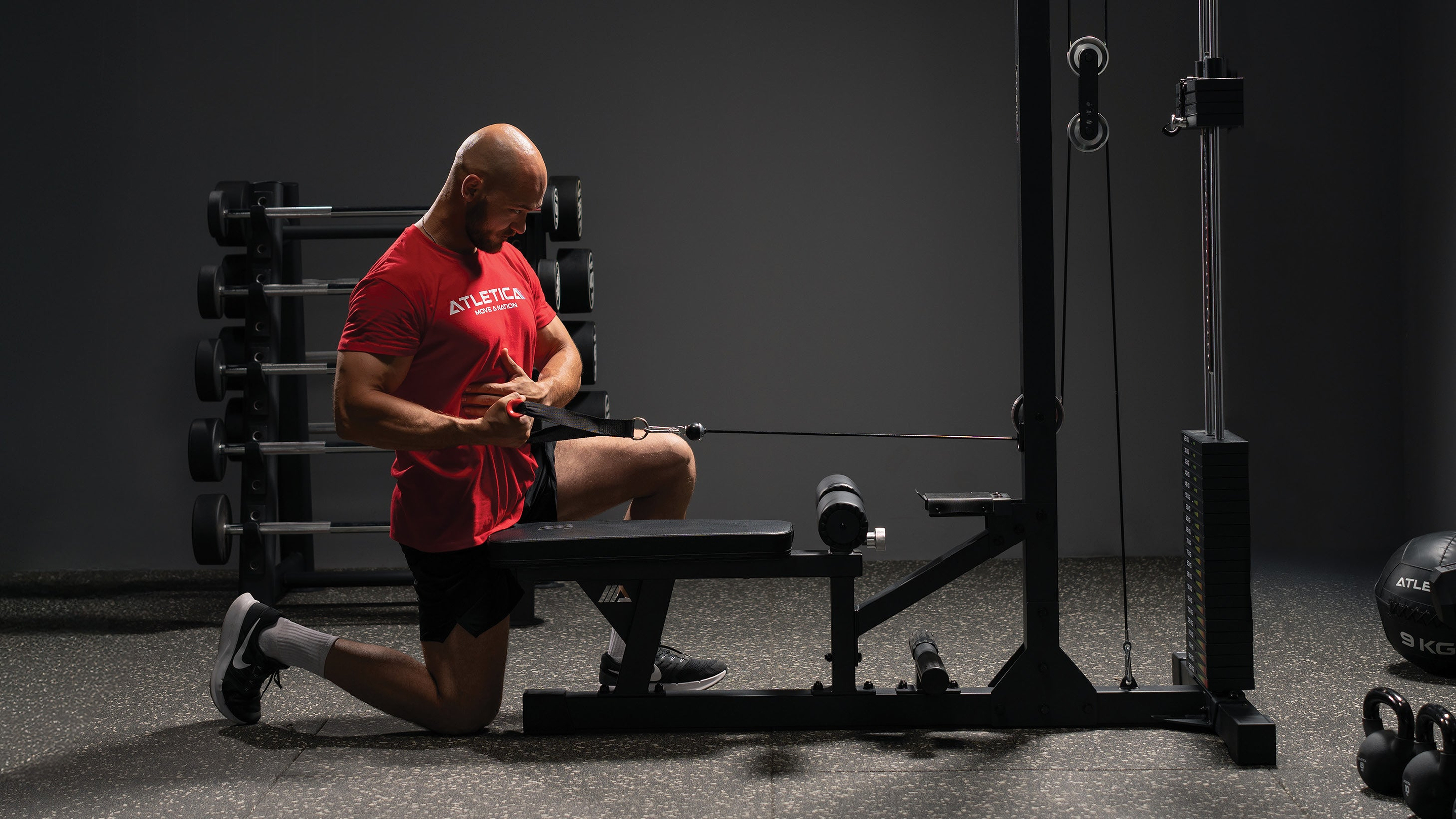 Homme faisant un rowing à un bras à genoux à la poulie Atletica dans son home gym