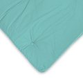 A teal cushion with a button in the center, resting on a white background with a slight wrinkle visible.