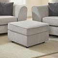 Thornby Standard Footstool Light Grey Charcoal from Roseland Furniture in a living room with the arm of a sof aon either sie, the room has white walls and light oak flooring covered by a cream rug.