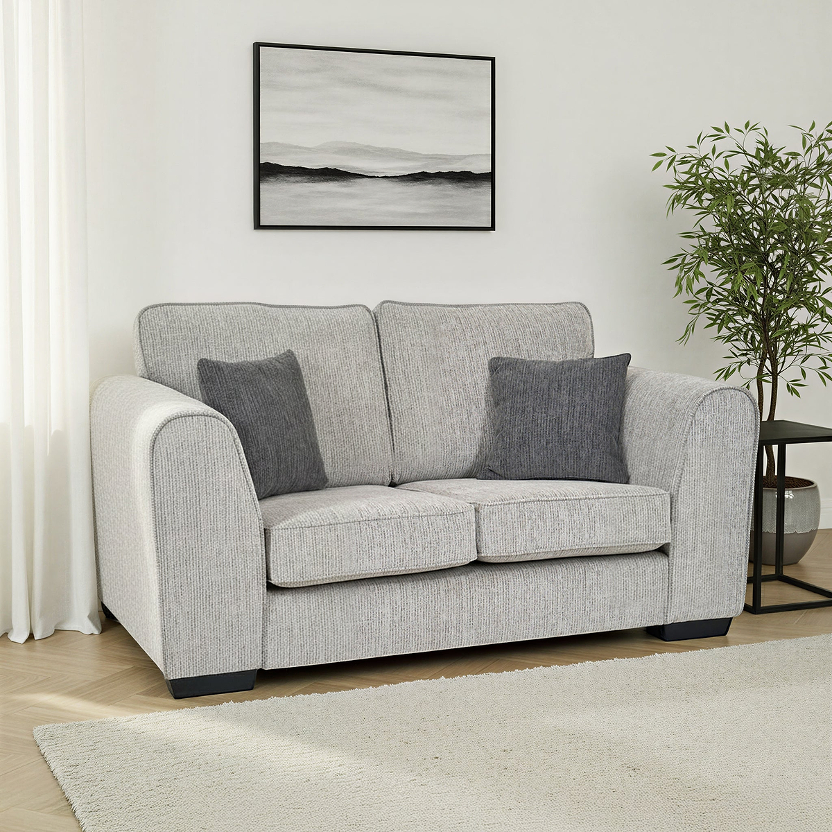 Thornby 2 Seater Sofa Light Grey Charcoal from Roseland Furniture in a living room adjacent to a window in a lounge with white walls and light oak flooring with a cream colour rug. to the right is a back side table and a tree and above is an abstract painting.