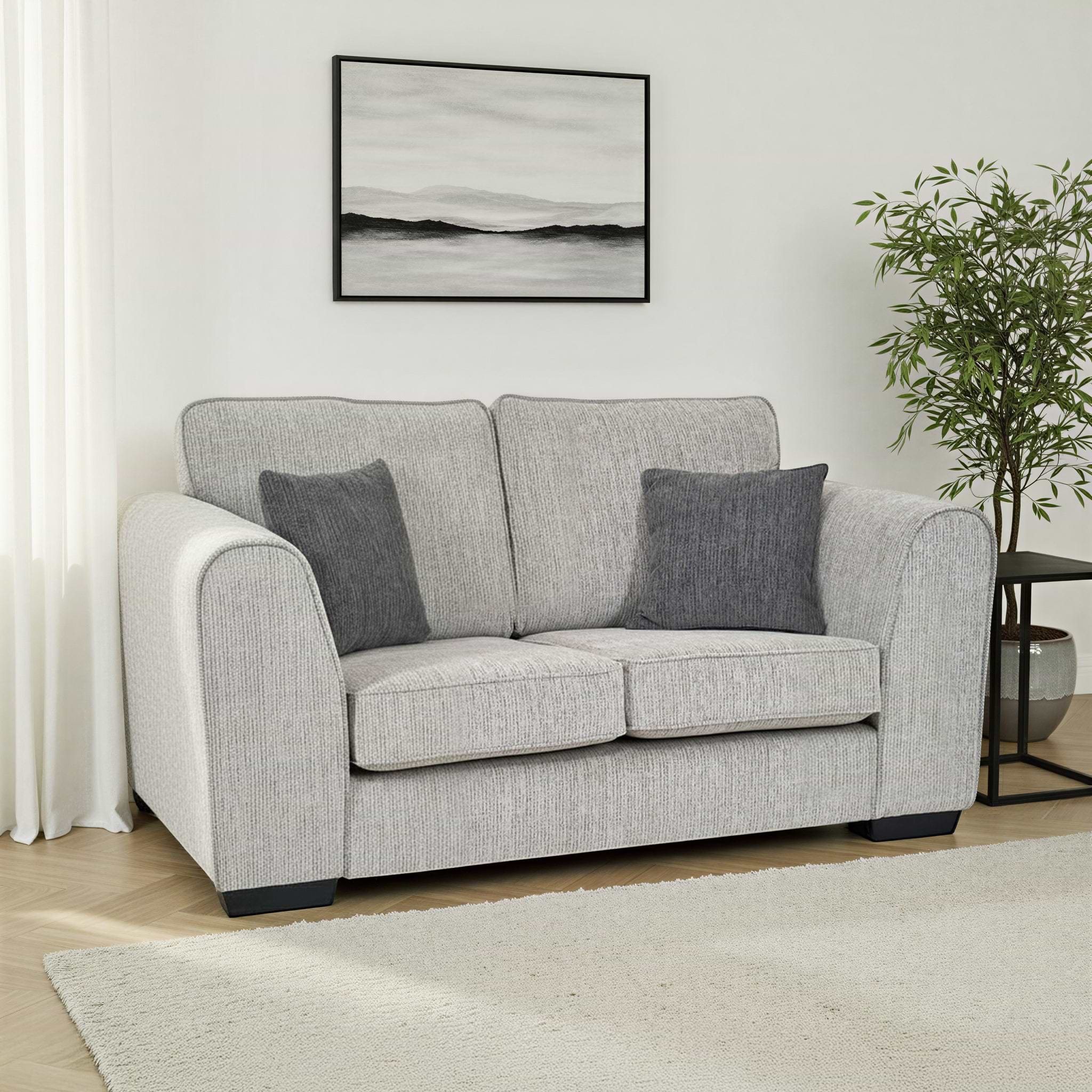 Thornby 2 Seater Sofa Light Grey Charcoal from Roseland Furniture in a living room adjacent to a window in a lounge with white walls and light oak flooring with a cream colour rug. to the right is a back side table and a tree and above is an abstract painting.