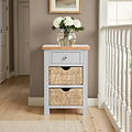 A small wooden storage cabinet with a drawer and two wicker baskets in a hallway with a vase of flowers on top