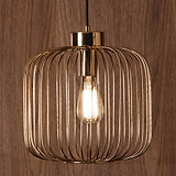 A gold-finished pendant light with vertical slats encasing an illuminated bulb, suspended against a wood-grain background.