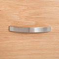 A curved metal handle is centered on a textured wooden surface, likely representing a piece of furniture or cabinetry.