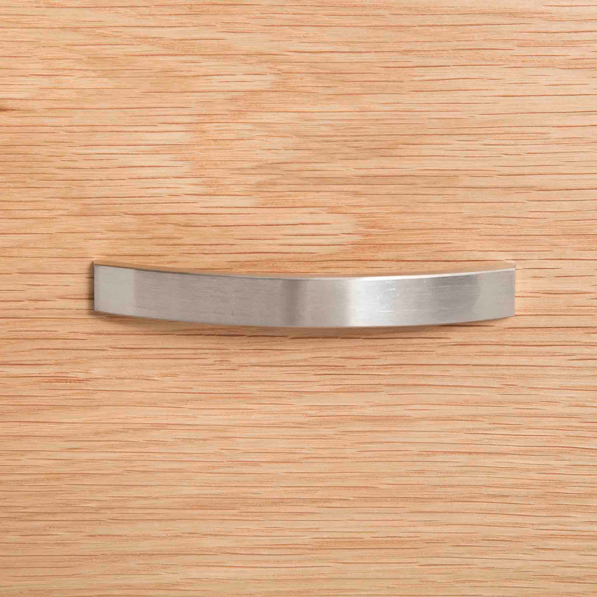 A curved metal handle is centered on a textured wooden surface, likely representing a piece of furniture or cabinetry.