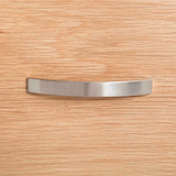 A curved metal handle is centered on a textured wooden surface, likely representing a piece of furniture or cabinetry.