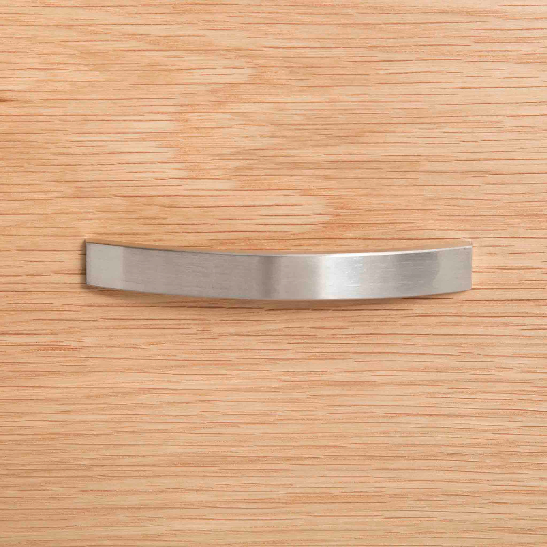 A curved metal handle is centered on a textured wooden surface, likely representing a piece of furniture or cabinetry.