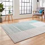 A modern rug with green and turquoise stripes lies on a wooden floor, flanked by minimalist furniture and large windows with a city view.