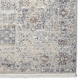 A textured rug features a distressed pattern in shades of beige, gray, and brown, with fringe on one edge.