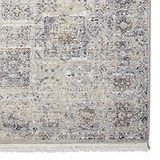A textured rug features a distressed pattern in shades of beige, gray, and brown, with fringe on one edge.
