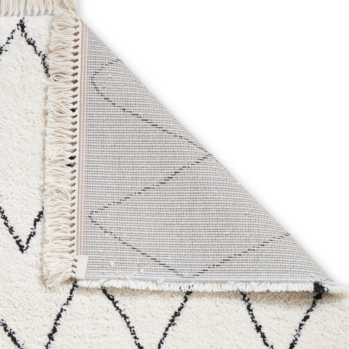 A beige and black patterned rug folded over a plain grey surface, showing geometric designs and fringe detailing.