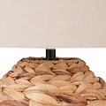 Close-up of a woven natural fiber lamp base with a black central stem and a beige fabric lampshade partially visible against a white background.