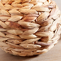 A close-up of a round woven basket made from natural water hyacinth fibers, showing the textured interlaced weave on a light wood surface.