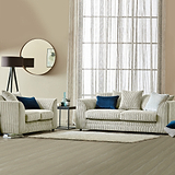 Striped sofa and armchair with blue and white cushions, a floor lamp, and round mirror, in a neutral-toned living room with sheer curtained window and wooden floor.