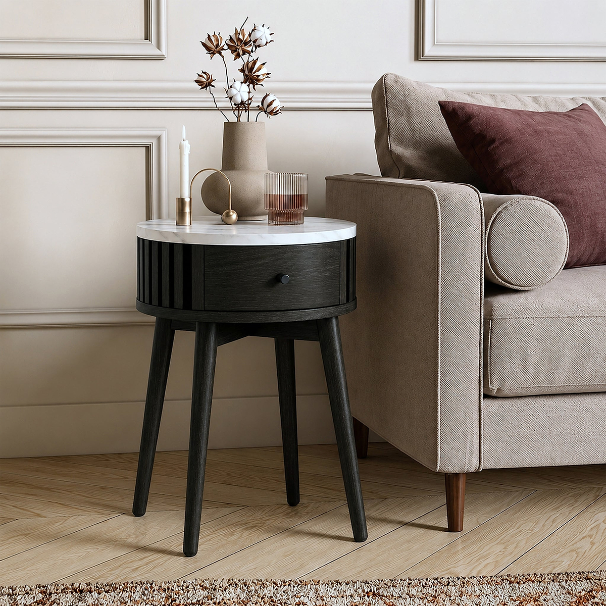 A modern Shorwell Black & Marble 1 Drawer Side Table with a white marble top and a dark charcoal black drawer and legs, styled next to a beige armchair in a living room setting.