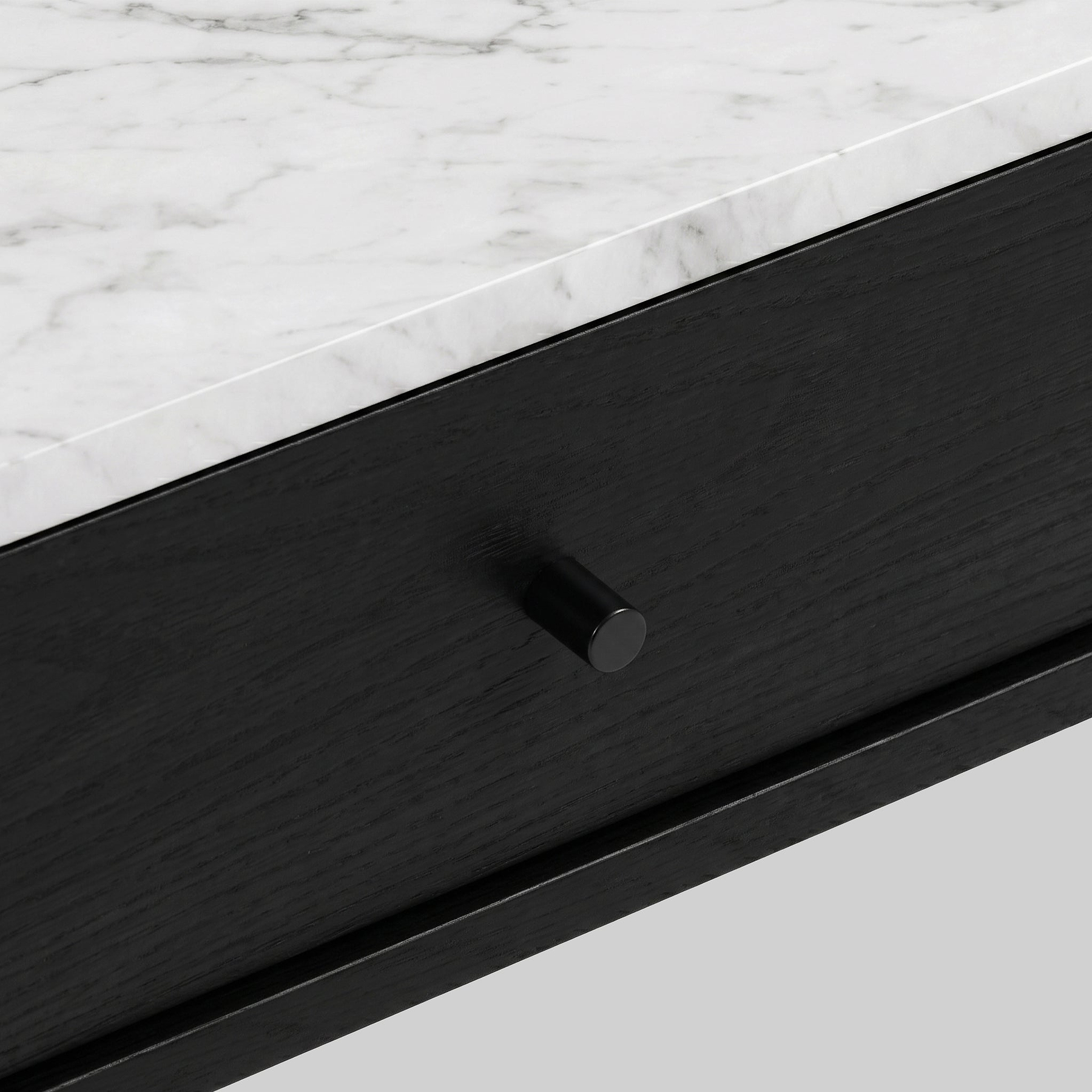 Close-up of a modern Shorwell Black & Marble 1 Drawer Oval Coffee Table drawer with a black wood finish and a small round black knob, set beneath a white marble top with gray veining.