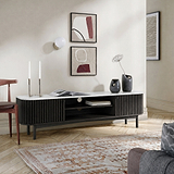 A modern Shorwell Black & Marble Slatted 180cm TV Unit in a styled living room setting, featuring a white marble-look top, a black ribbed cabinet body, and open shelving.