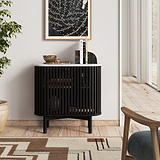 A modern Shorwell Black & Marble Cupboard with vertical slats, a white marble top, and tapered black legs, styled in a bright living room setting.