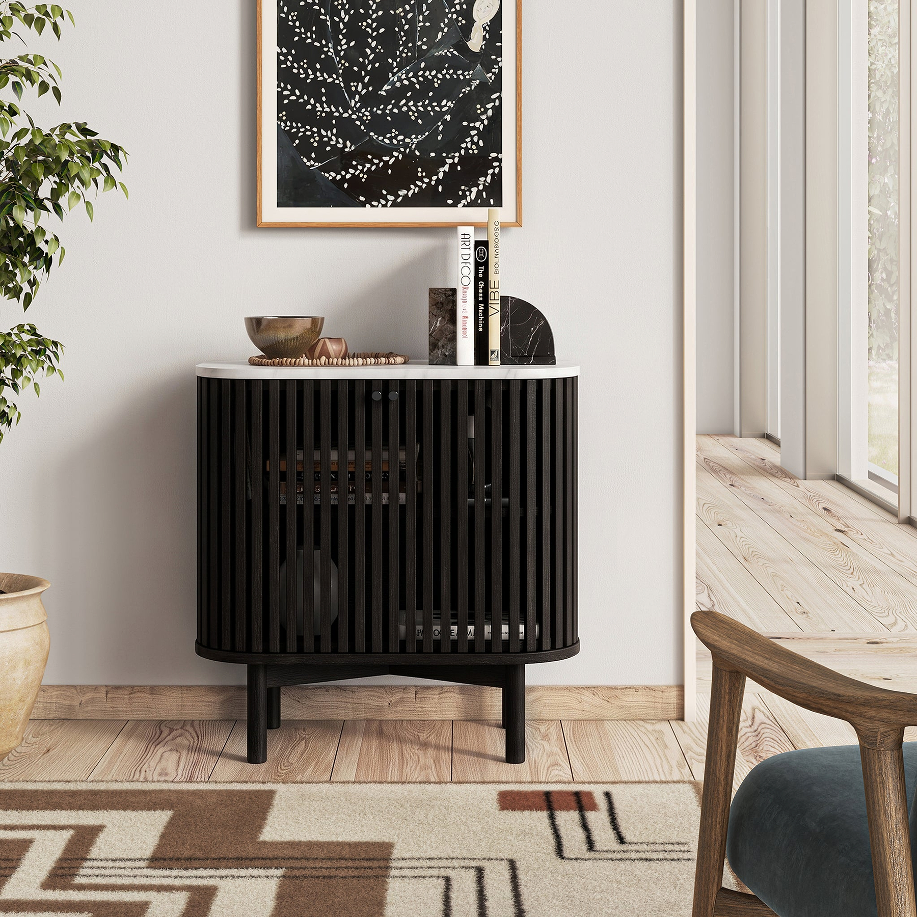 A modern Shorwell Black & Marble Cupboard with vertical slats, a white marble top, and tapered black legs, styled in a bright living room setting.