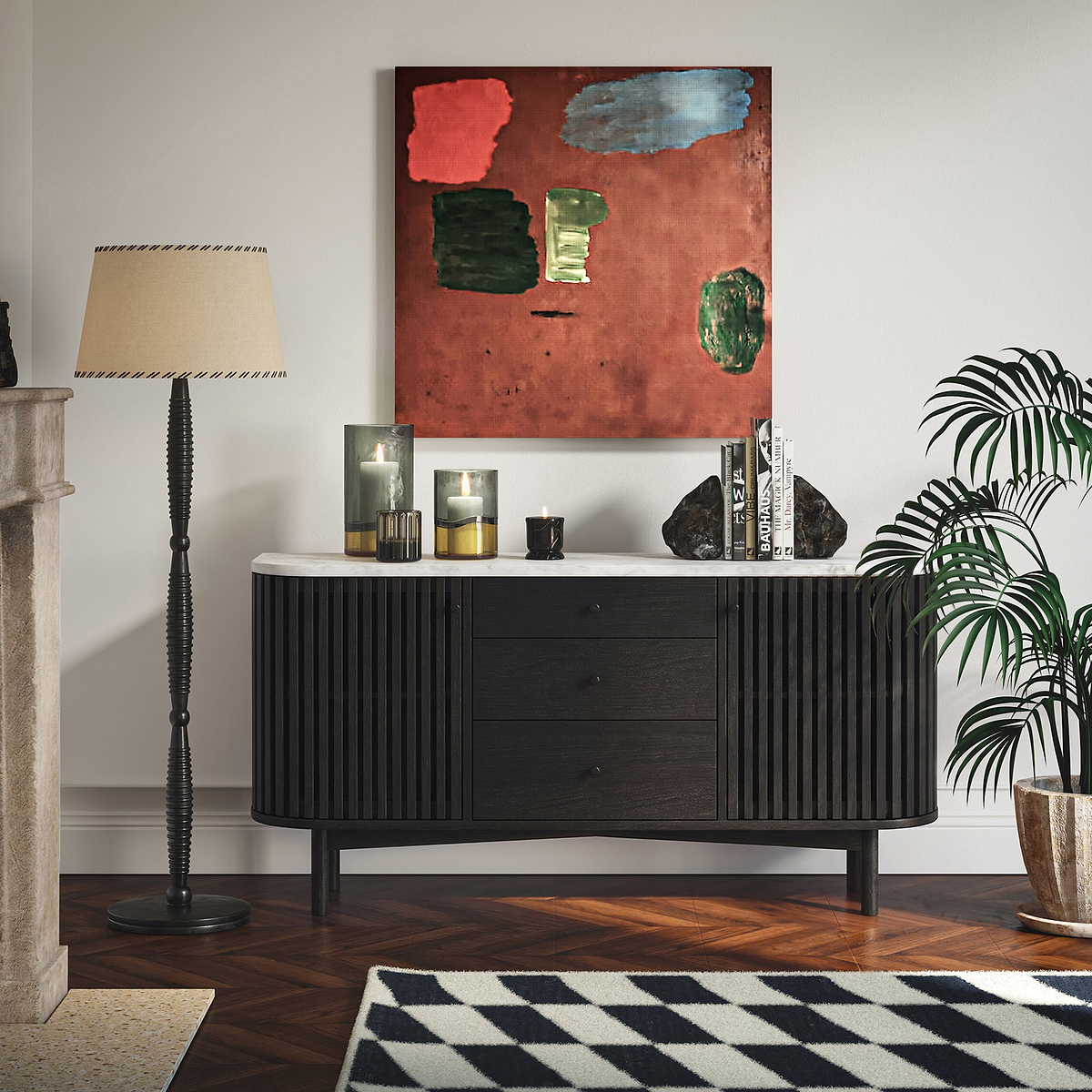 A modern Shorwell Black & Marble 3 Drawer Sideboard with a white marble top, styled in a living room setting with a black floor lamp, a potted palm, and an abstract painting on the wall.