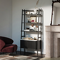 A Shorwell Black & Marble Bookcase with a slatted lower cabinet door, styled with books, vases, and decor in a modern living room next to a burgundy armchair and a stone fireplace.