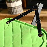 A black strap attached to a lime-green quilted fabric with a metal ring, likely part of a bag or furniture, in a wooden interior setting.