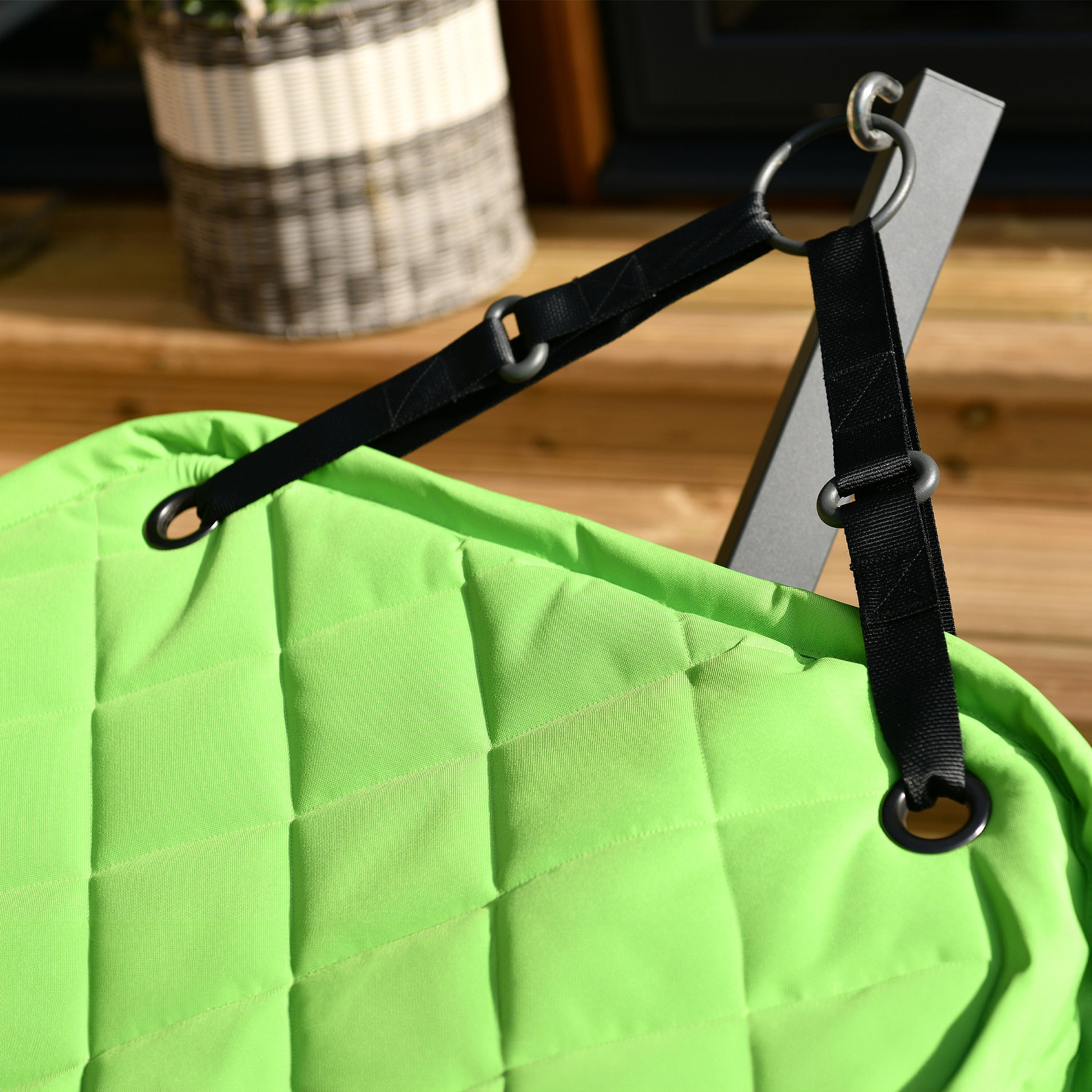 A black strap attached to a lime-green quilted fabric with a metal ring, likely part of a bag or furniture, in a wooden interior setting.