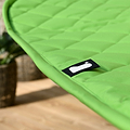 A close-up of a bright green, quilted fabric with a black label featuring a white design, possibly indicating a brand, placed on a blurry indoor background.