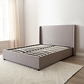 Brent Ottoman Storage Bed Frame from Roseland Furniture- Gray upholstered bed in a minimalistic bedroom setting with light-colored walls and wooden flooring.