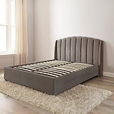 Gray upholstered bed in a room with a window and beige curtains.