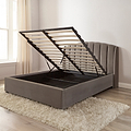 Gray upholstered bed with storage compartment in a room with a window and rug.