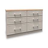 A wooden six-drawer dresser with a light brown top and silver handles sits idle in a white void.