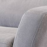 Close-up of a grey fabric sofa showcasing texture, with focus on the armrest and cushion in a home interior setting. No text present.