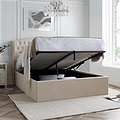 A natural upholstered ottoman bed with a lifted mattress reveals storage underneath, positioned against a paneled wall on a herringbone wood floor.