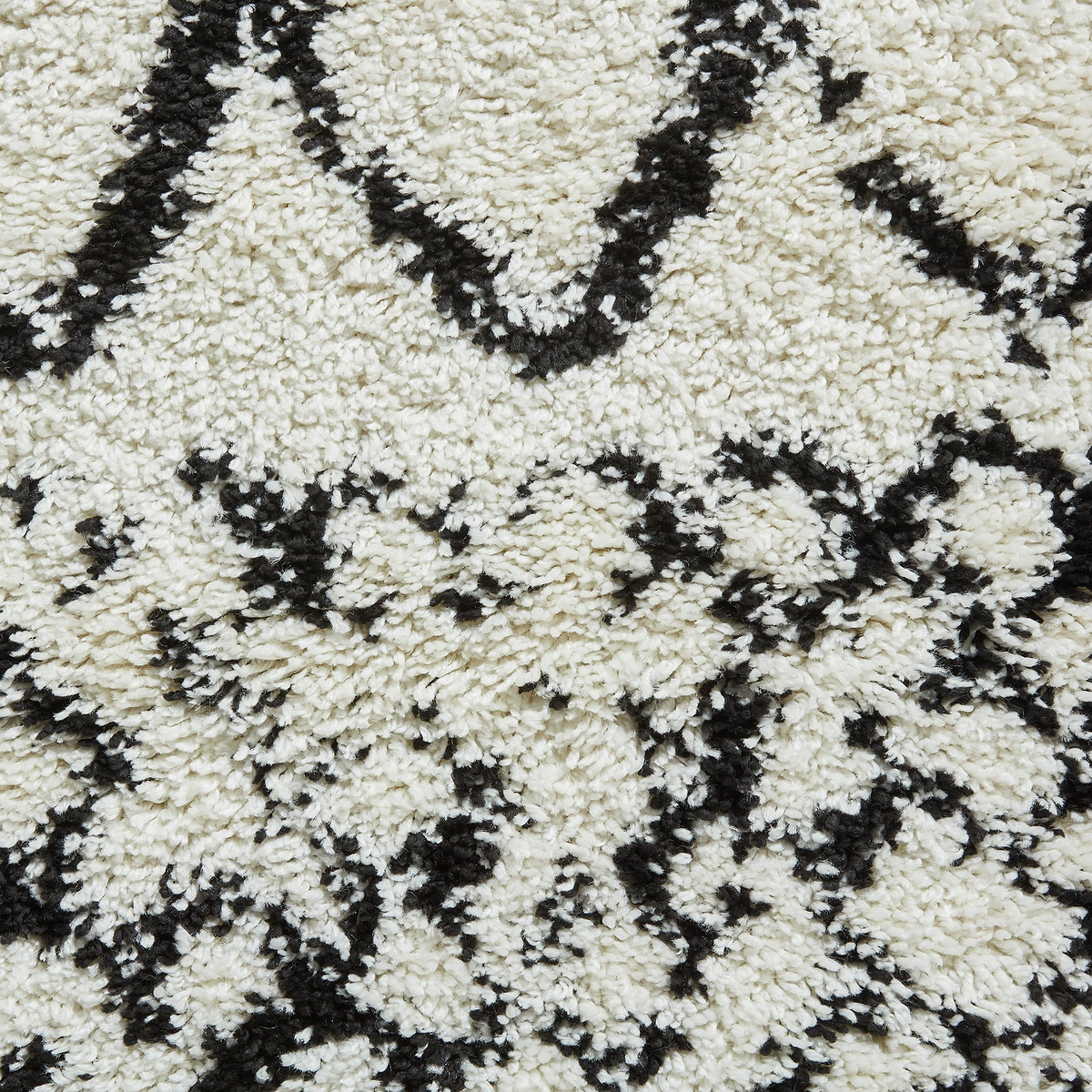 A close-up of a textured rug with a black and white geometric pattern, primarily featuring diamond shapes and zigzag lines.