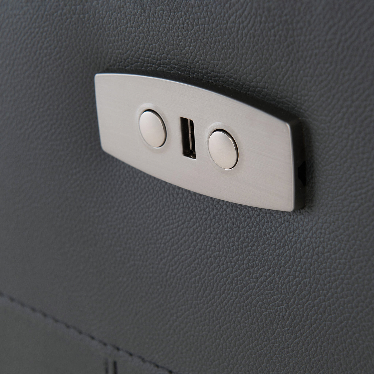 A metal clasp with two circular buttons on a textured gray surface, suggesting a piece of furniture or vehicle interior.
