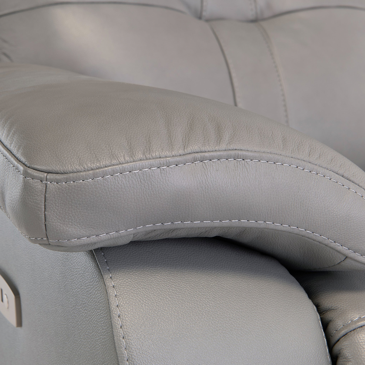 A close-up of a gray leather chair arm, highlighting the stitched details and plush padding, implying comfort and modern design.