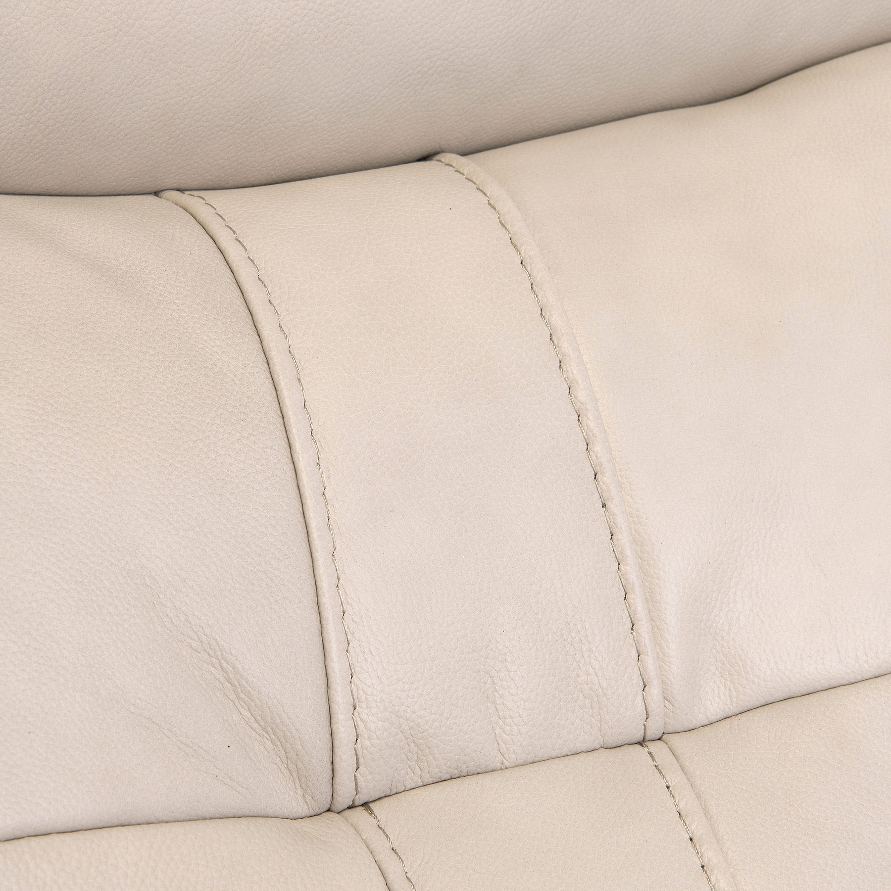 Close-up of a beige leather surface with visible stitching, likely a part of furniture such as a sofa or chair.