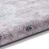 A patterned rug with a gradient from white to pink lies flat, showcasing traditional designs. The texture appears soft and plush.