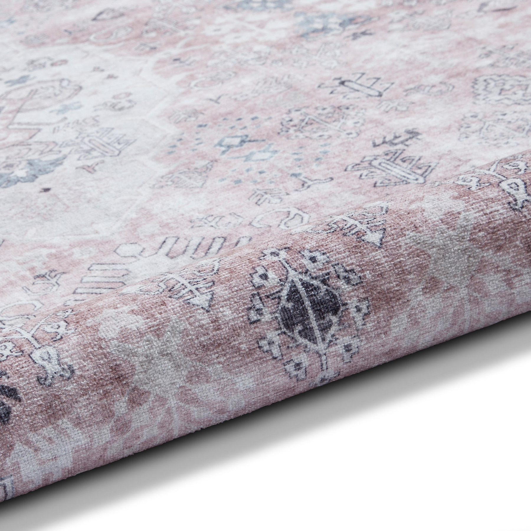 A patterned rug with a gradient from white to pink lies flat, showcasing traditional designs. The texture appears soft and plush.
