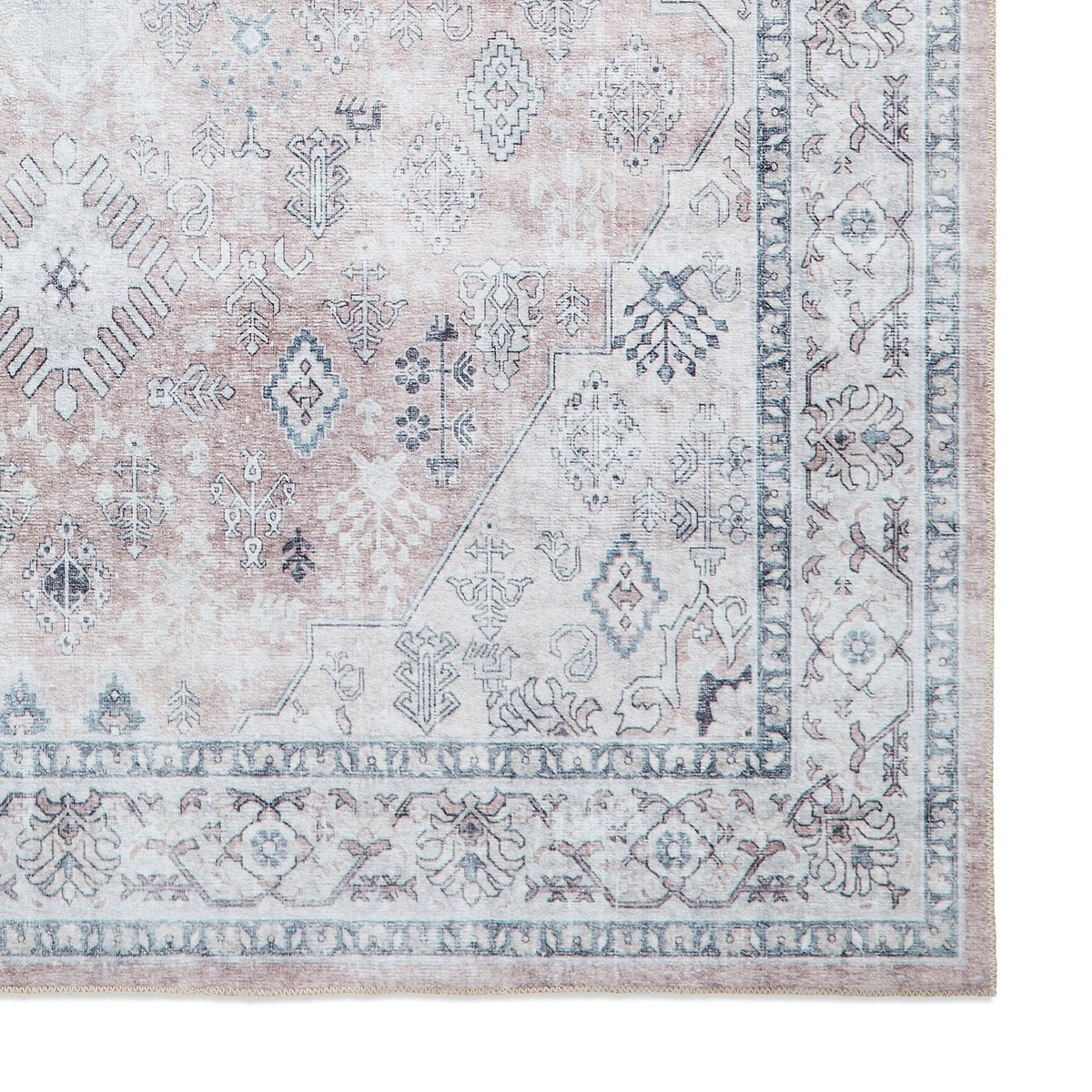 A patterned rug with geometric and floral designs rests flat, showcasing muted tones mainly in the grey and pale pink spectrum, creating a vintage aesthetic.