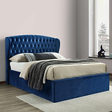 A blue, tufted headboard attached to a matching bed base with a white, quilted mattress in an elegant room with paneled walls and herringbone-patterned wooden floor.