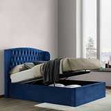 A blue upholstered storage bed with its mattress lifted to reveal an empty compartment underneath. It's situated in a room with paneled walls and herringbone wood flooring.