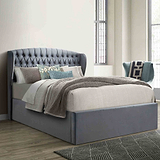 A gray upholstered bed with a tall, tufted headboard is set against a paneled wall on herringbone-patterned wooden flooring.