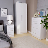 White bedroom furniture sits in a tidy room, with a wardrobe, a chest of drawers, and a nightstand. A framed quote reads "our happy place" on the wall.