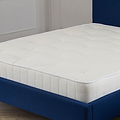 A white mattress on a blue bed frame set against a neutral wall and wooden flooring. No text is visible.